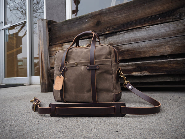 Light brown canvas briefcase measuring 15.5 inches length, 11.75 inches tall and 4.5 inches wide. Dark brown leather bottom. Two dark brown leather straps riveted to front pocket with copper rivets that become the handle. Dark brown leather handle wrap. YKK Brass zipper. Dark brown leather shoulder strap with copper rivets and antique brass swivel snaps.