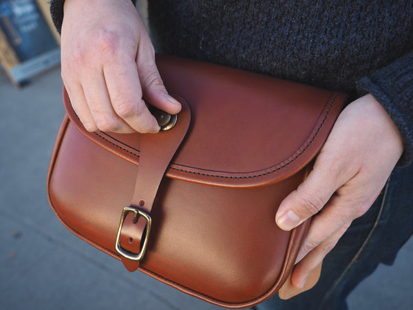 Brown leather purse with flap and leather binding.  Solid brass quick snap and rounded buckle.