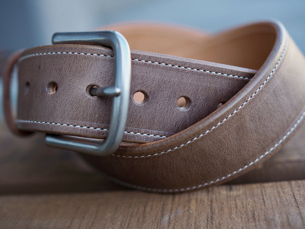 Light brown leather belt with white border stitch and rounded matte nickel buckle and seven adjustment holes.